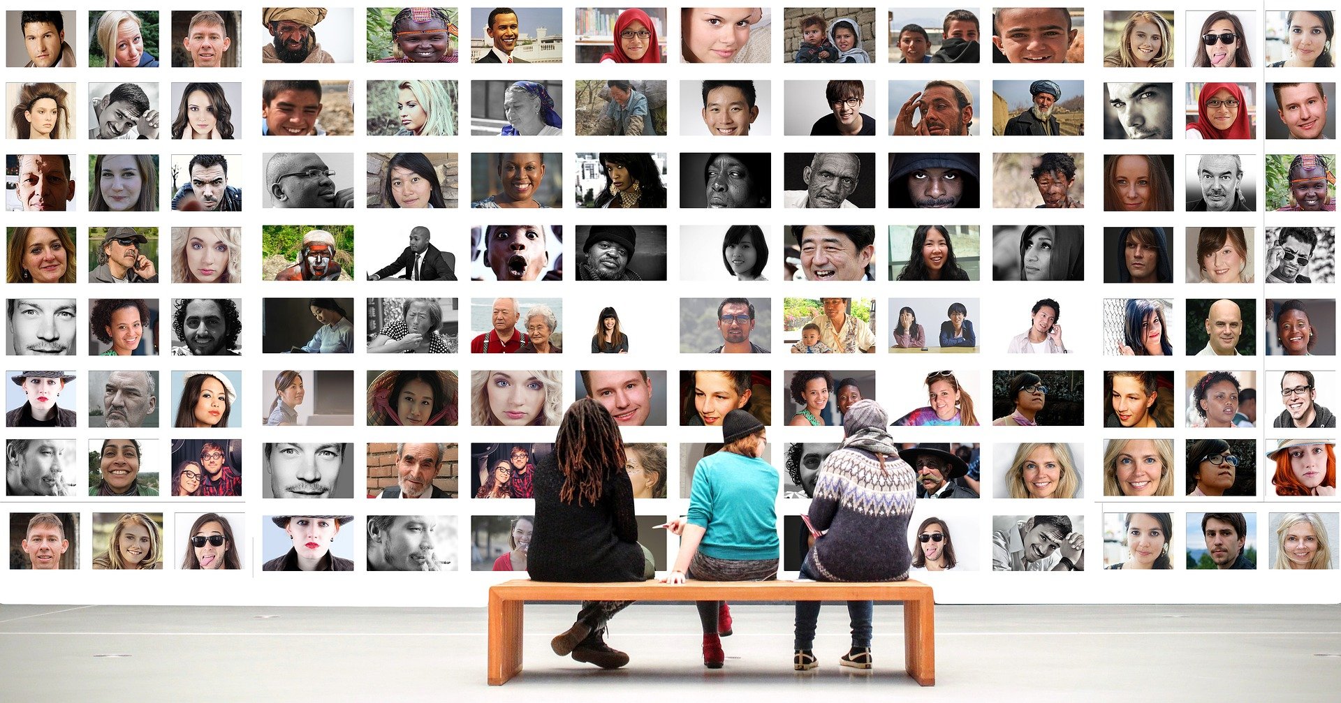 Three people sitting on a bench looking at a large collage of profile pictures of diverse people