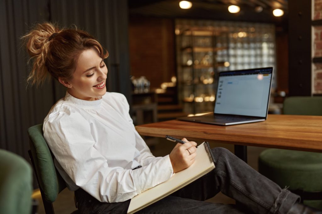 Smiling woman taking notes while working on laptop